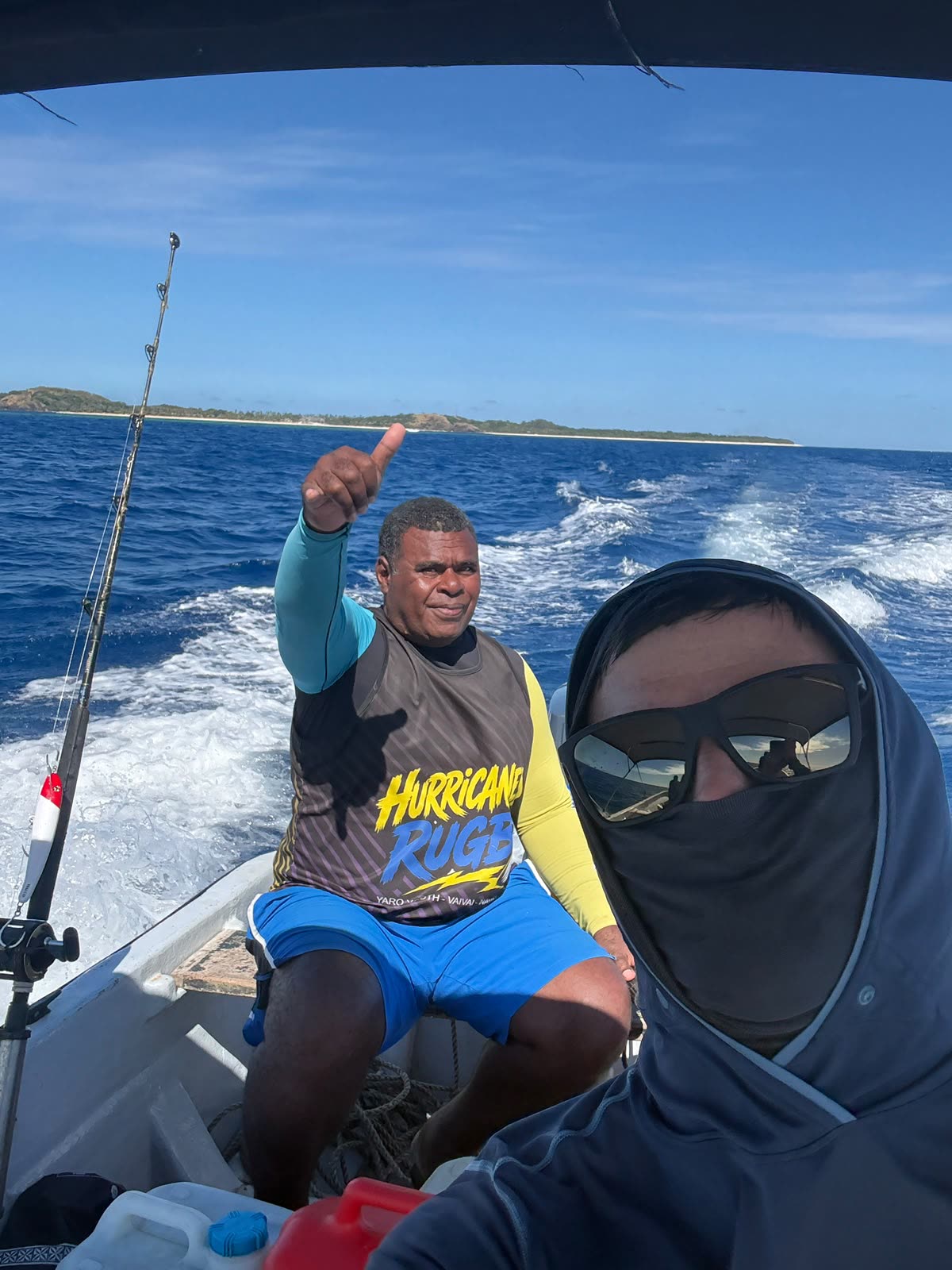Guests on the boat mid-trip, fishing rod in hand, Mamanuca island in the background