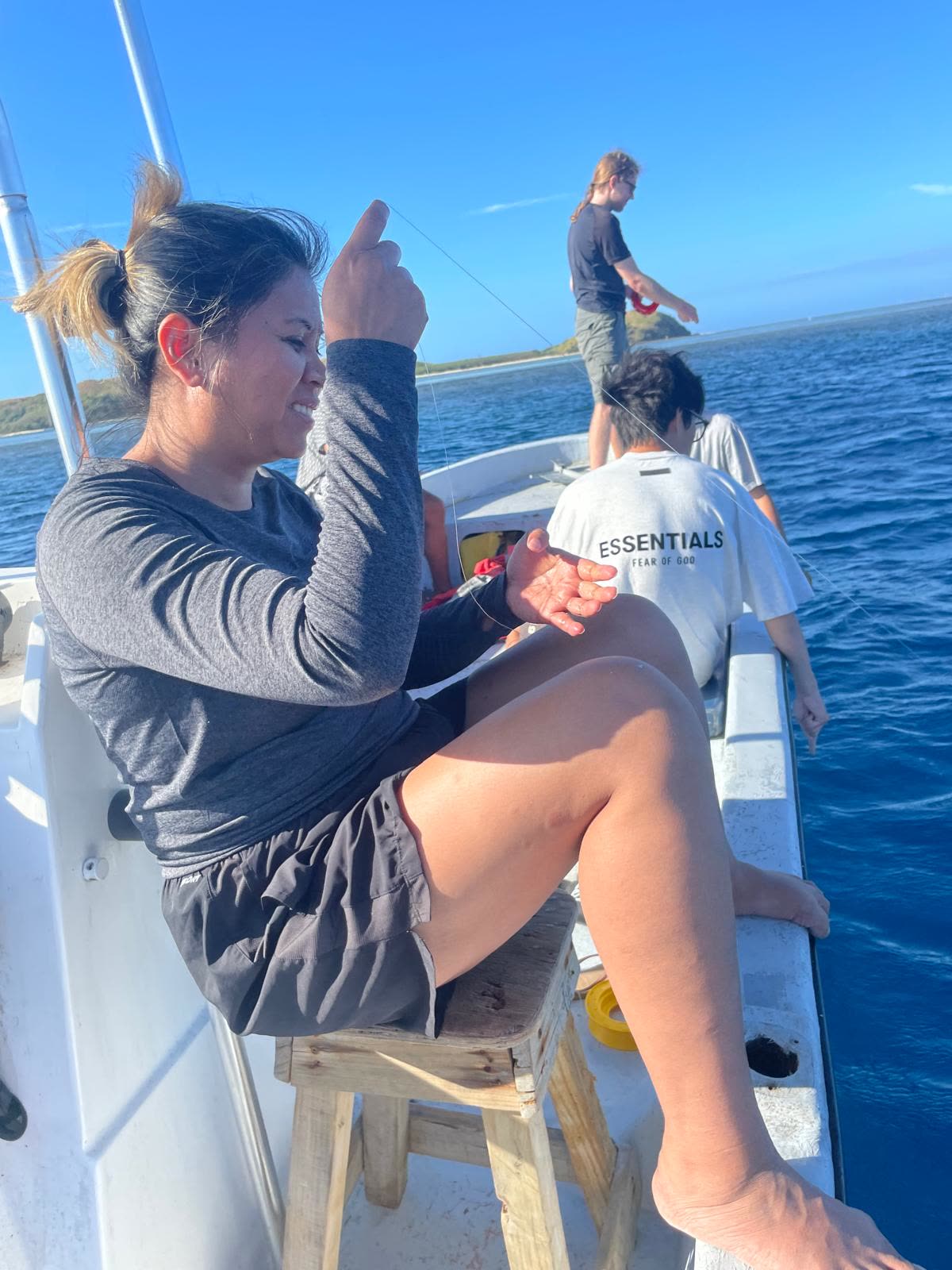 Guest handling fishing line aboard the boat while others fish nearby, blue island water all around