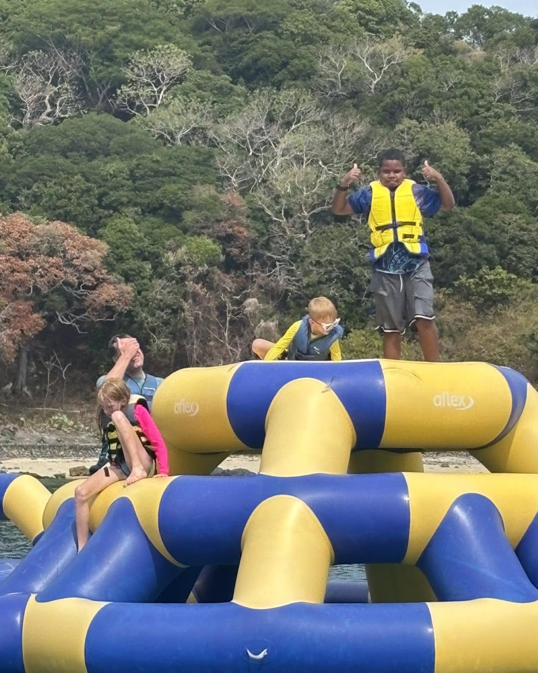 Kids playing on an inflatable water trampoline just off the beach, life jackets on