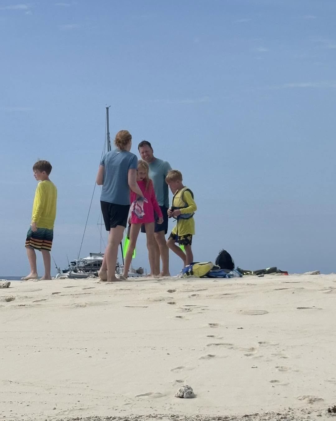 Family with snorkel gear on a sandbar, sailboat anchored behind them